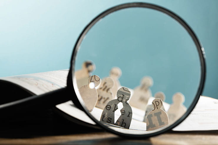 Concept of recruitment; candidate icons made out of newspaper under a magnifying glass. 